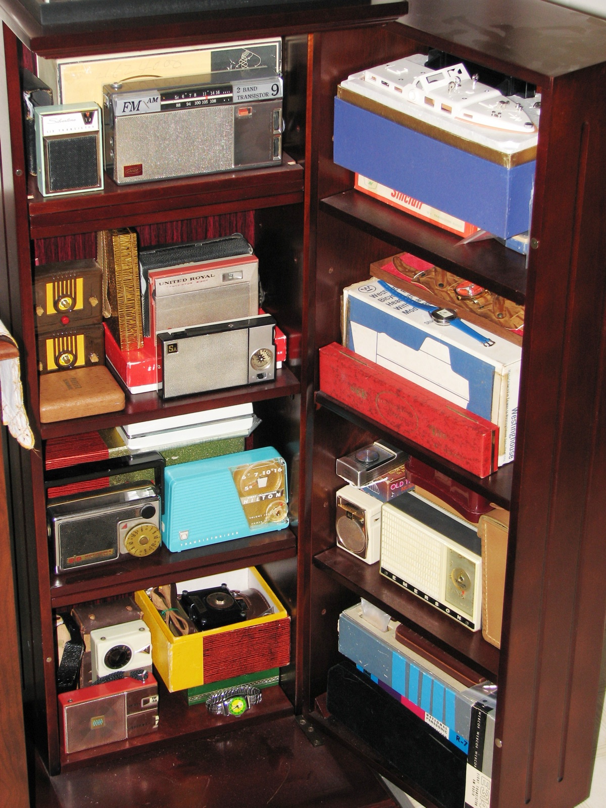An open wooden cabinet with several old transistor radios in different colours on its shelves