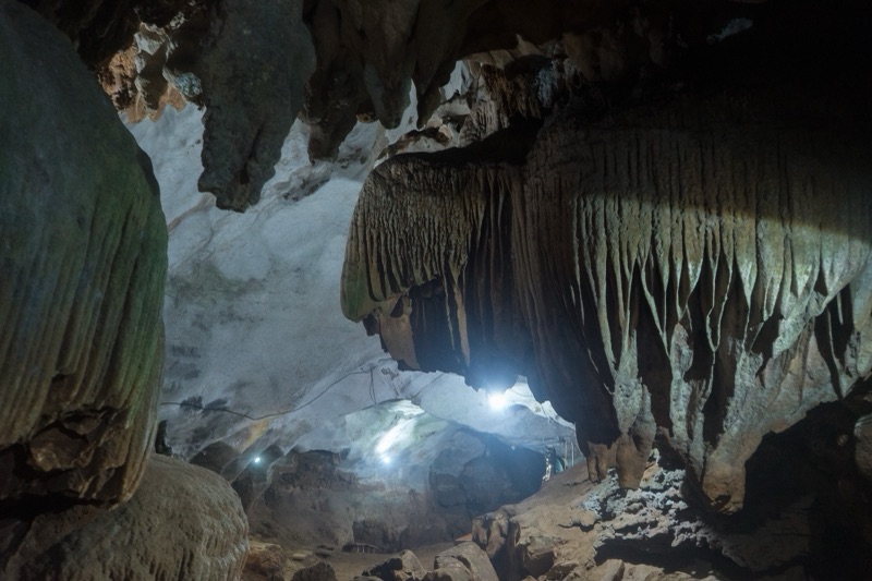 Inside Chiang Dao Cave: curtain-like stalactites hang from the cave roof, with light shining from a deep passage beyond