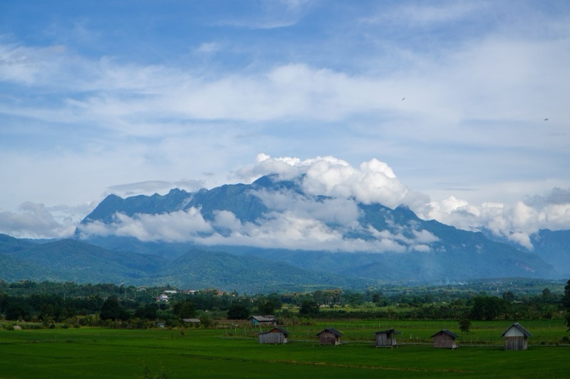 Doi Luang Chiang Dao, a towering limestone mountain with white clouds over its peak, above green rice fields and small field huts