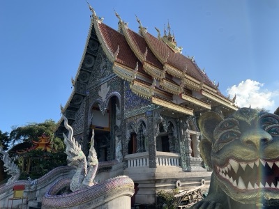 The ordination hall of Wat Phra That Doi Khao Khwai Kaeo with tiered Lanna roofs, naga balustrades and the head of the Maeng Si Hu Ha Ta statue on the right