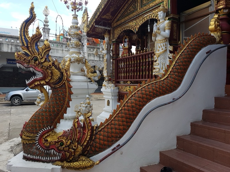 ราวบันไดรูปพญานาคสีทองลายเกล็ดสีส้มแดง เลื้อยลงมาตามขั้นบันไดหน้าวิหารวัดมิ่งเมือง เชียงราย หัวนาคอ้าปากชูหงอนสูง