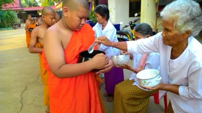 สามเณรอุ้มบาตรรับข้าวจากหญิงสูงวัยที่นุ่งขาวห่มขาว