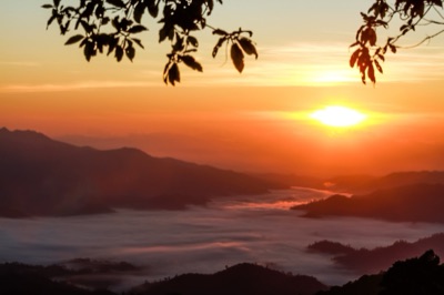 An orange sun rising over a sea of mist and mountain ridges