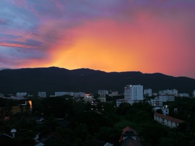 A red-orange sky at sunset behind Doi Suthep, with Chiang Mai buildings below