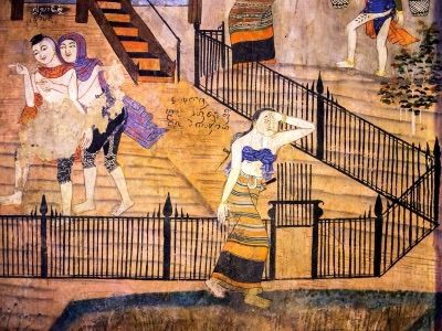 Wat Phumin mural: a woman in a striped sin with a cloth tied across her chest walks past a fence