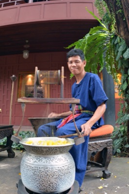 A man in a blue shirt with a checked cloth at his waist reels silk from a pot of yellow cocoons