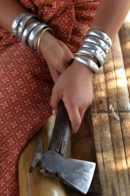 A woman's wrists stacked with thick silver bangles, her hand on an axe handle