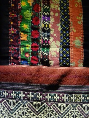 Colourful Tai Lue textile in joined bands, with a white geometric pattern on a dark ground below