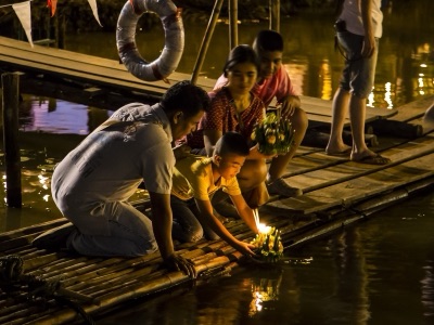 ครอบครัวหนึ่งกำลังวางกระทงจุดเทียนลงในแม่น้ำปิงยามค่ำคืน