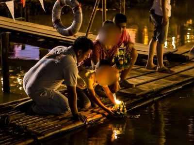 ครอบครัวหนึ่งกำลังวางกระทงจุดเทียนลงในแม่น้ำปิงยามค่ำคืน