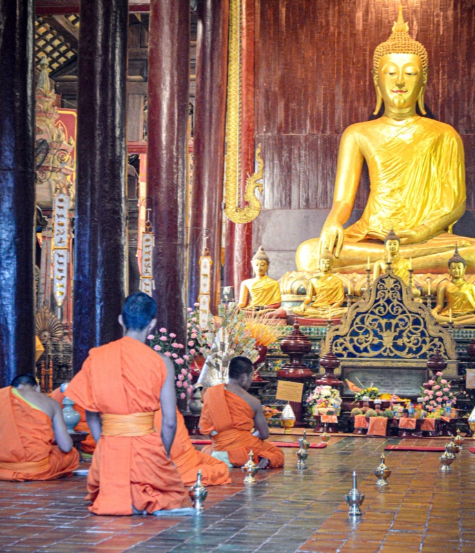 สามเณรและพระภิกษุนั่งพับเพียบหน้าพระประธานในวิหารวัดที่เชียงใหม่