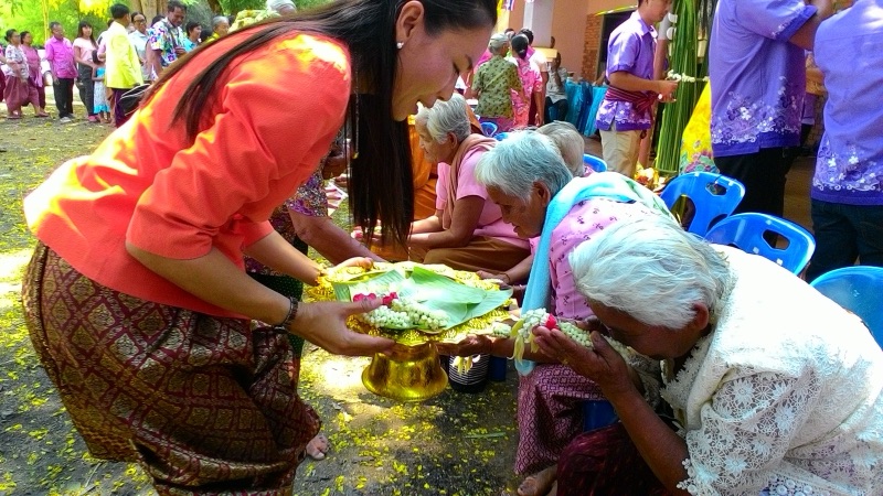 หญิงสาวนุ่งผ้าซิ่นยื่นพานใบตองให้ผู้สูงอายุที่นั่งรอรับพรในงานสงกรานต์