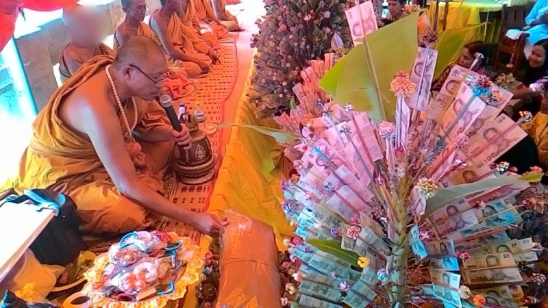Monks chanting beside a merit-making tree decorated with banknotes and flowers, at a temple in Nakhon Ratchasima province