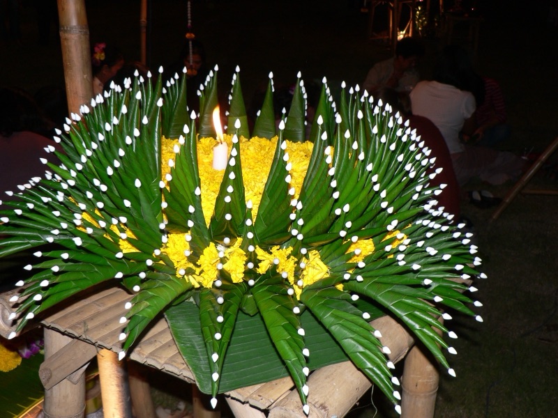 A krathong of banana leaves folded into pointed cones in a ring, decorated with yellow flowers and a candle in the middle, on a bamboo stool on Loy Krathong night in Chiang Mai