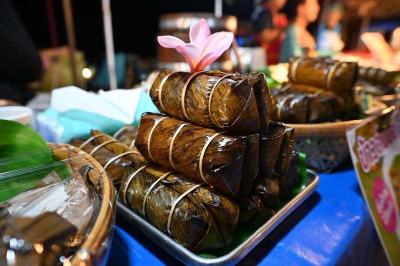 Sticky rice parcels wrapped in banana leaf and tied, stacked on a tray with a pink flower on top