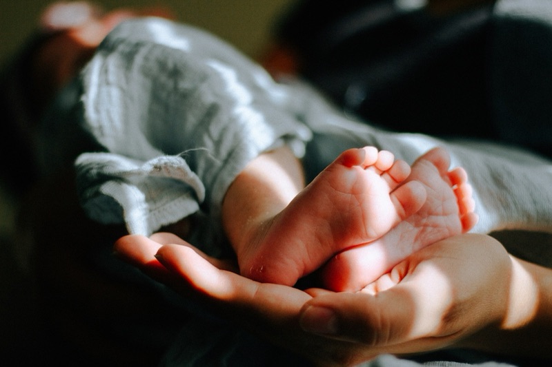 An adult's hand cradling a baby's tiny, chubby feet